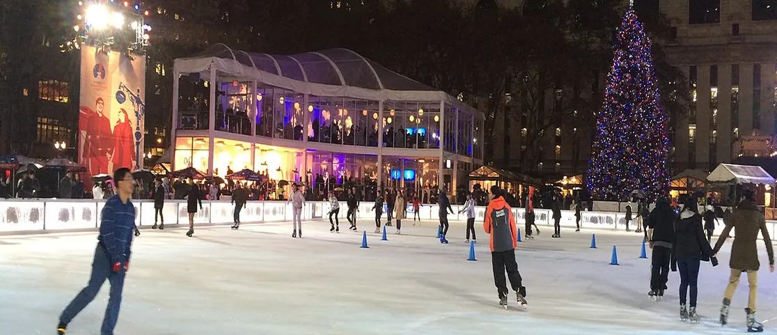 Glowing holiday market at night with illuminated kiosks, Christmas tree, and shoppers in Manhattan