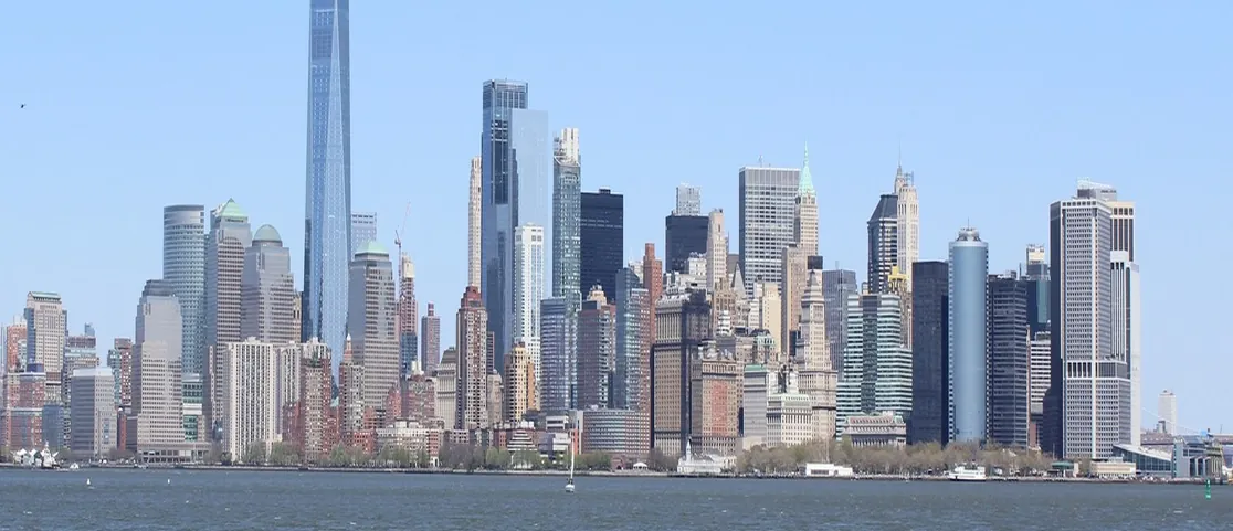 Modern glass hotel tower and waterfront promenade in Battery Park City overlooking Hudson River skyline