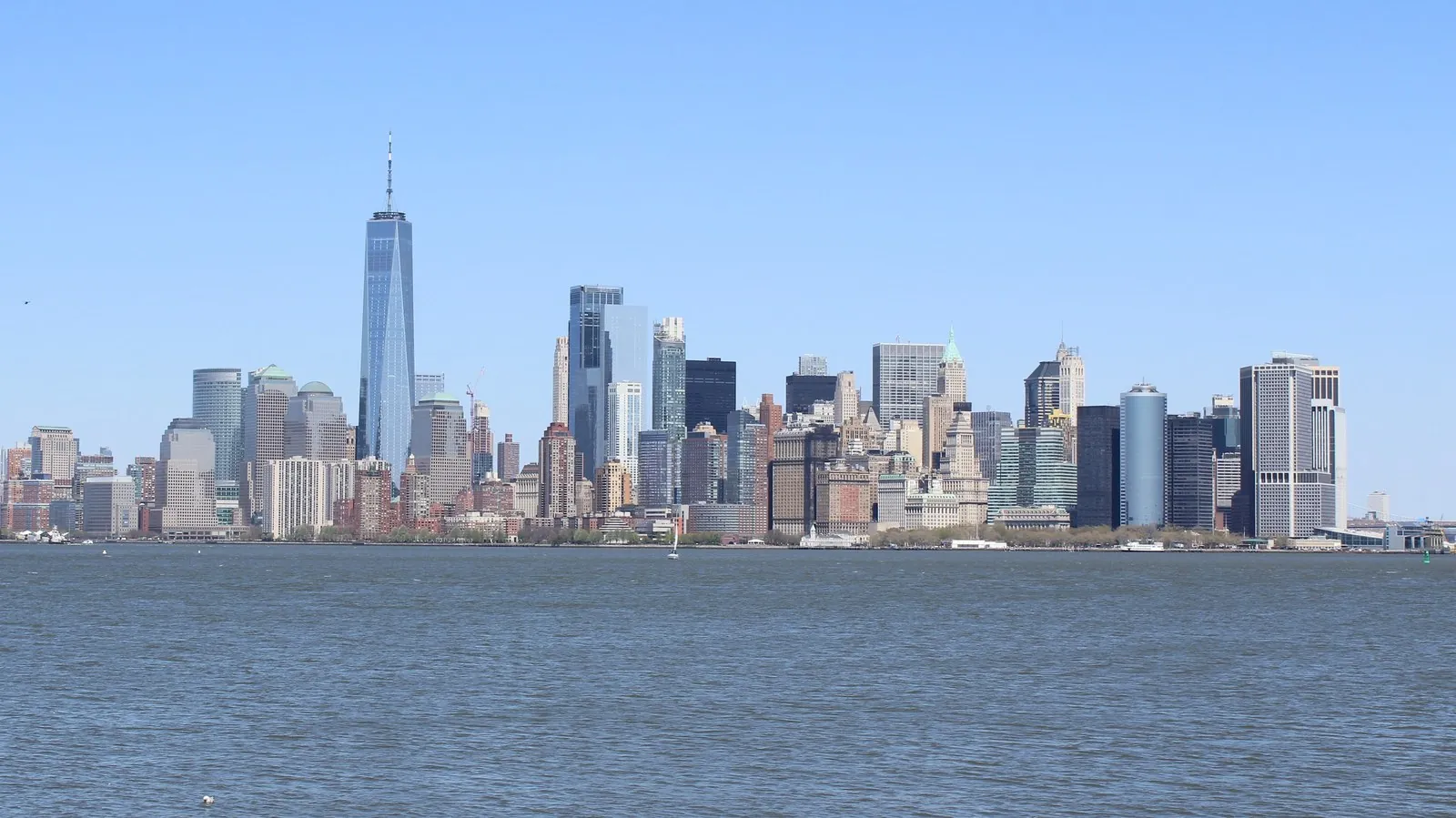 Panoramic Lower Manhattan skyline view showing One World Trade Center and Financial District towers from Liberty Island.