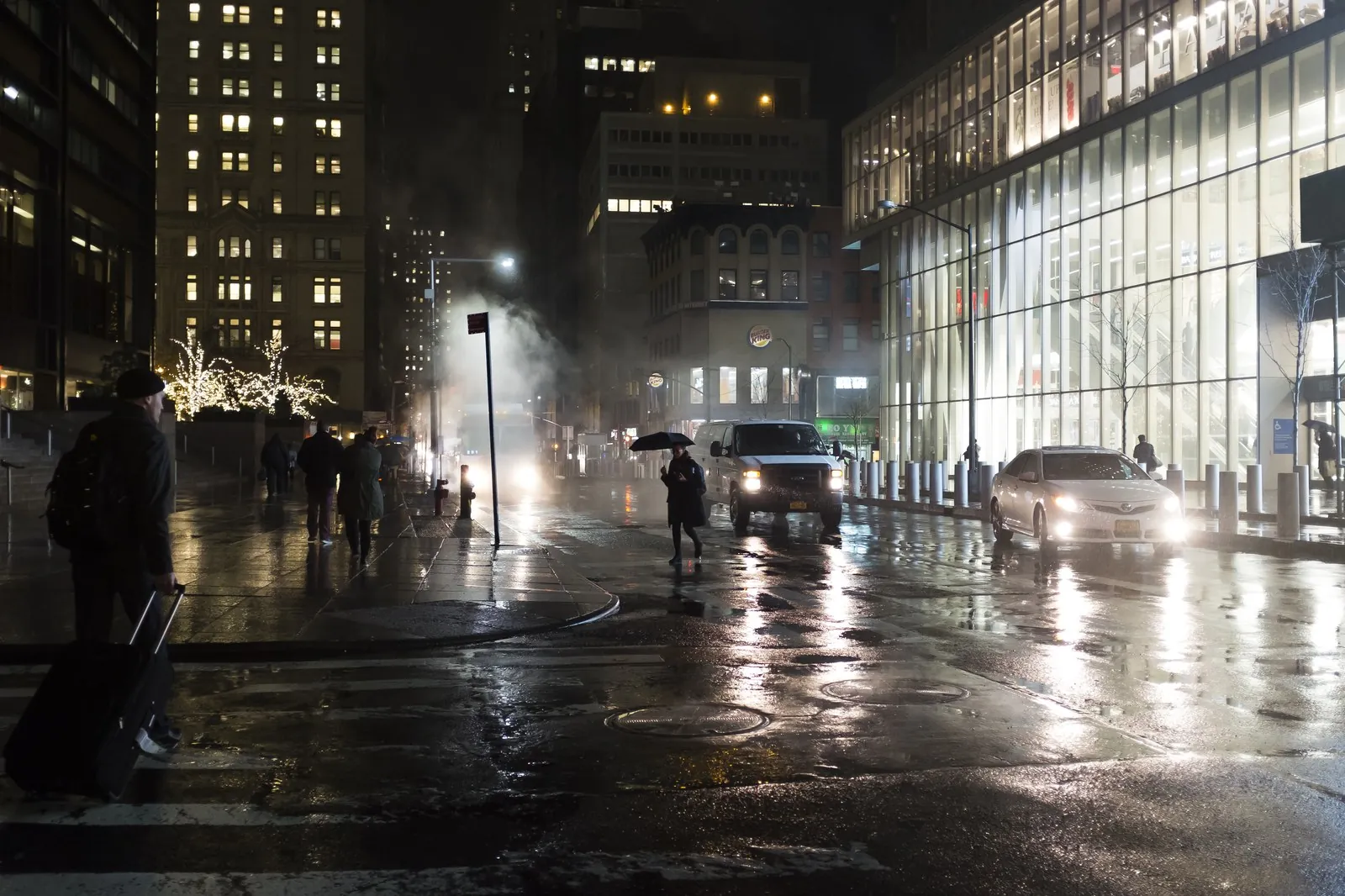 Atmospheric rainy evening view of Manhattan street and building lights reflected on wet pavement.