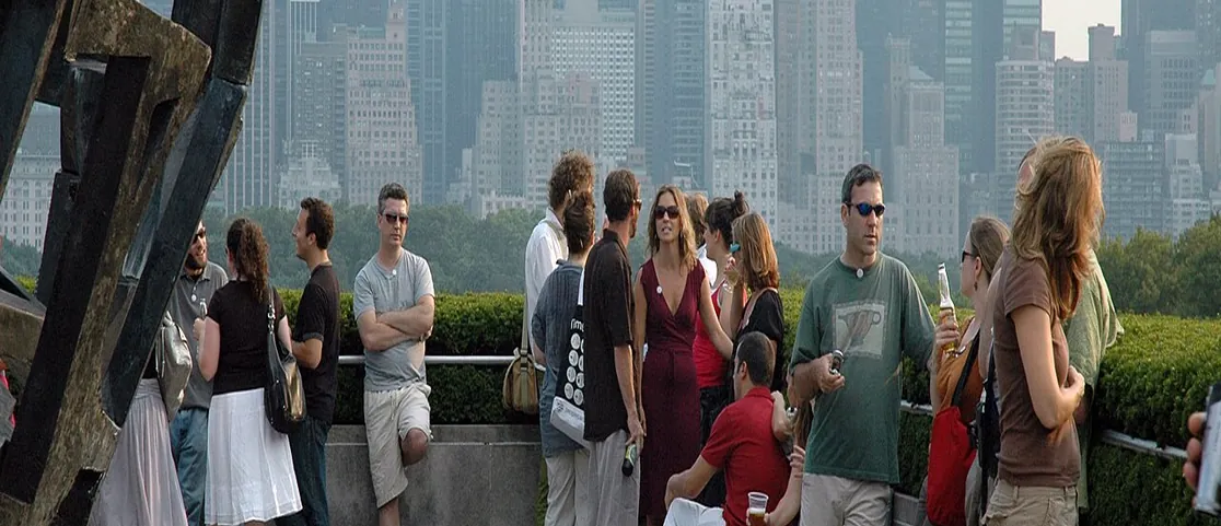 People enjoying drinks at a bustling open-air rooftop bar in New York City