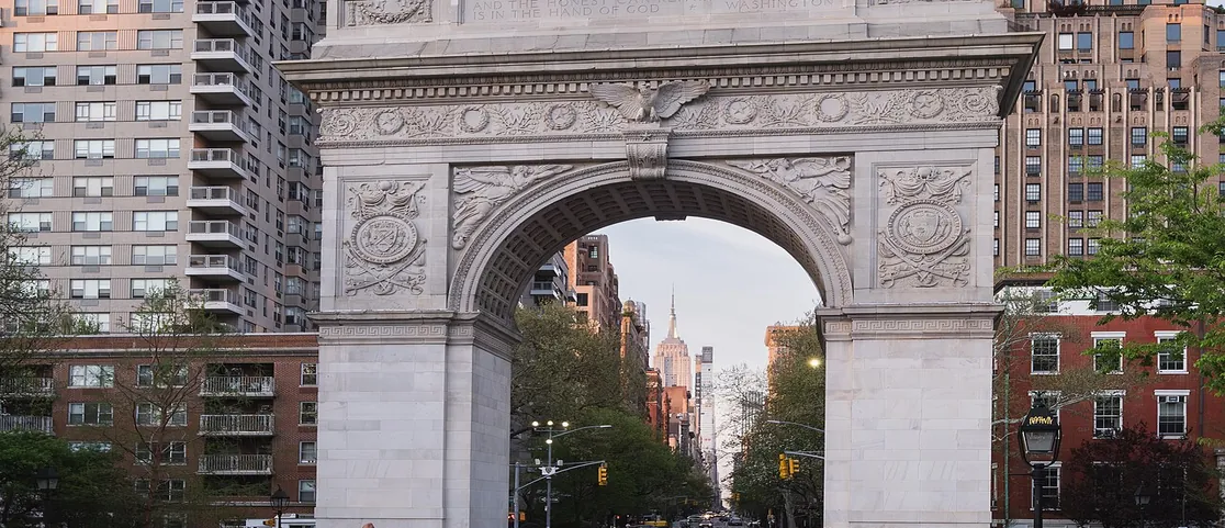 Washington Square Arch in Greenwich Village framed by green spring trees and the Empire State Building