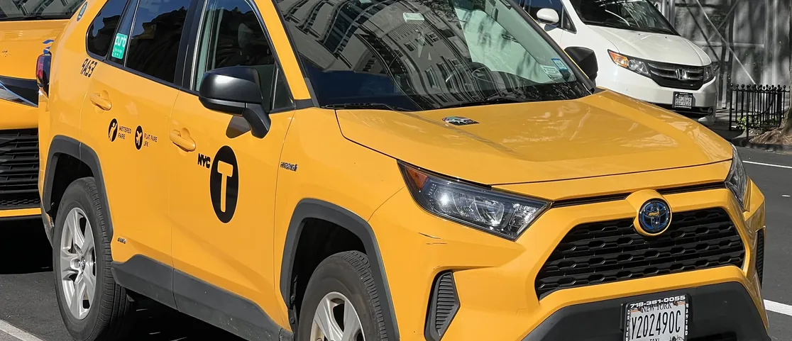 Yellow cab driving on a busy Manhattan street with NYC medallion taxi signage